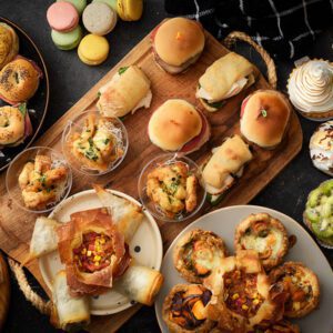 Mesa con productos de catering: tartines, tartas dulces, sandwiches, chicken fingers y macarrons